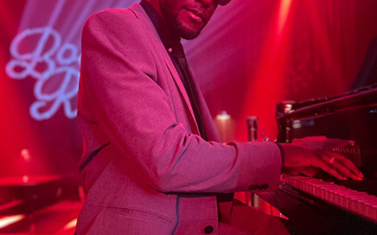 Timothonius wearing sunglasses playing the piano in dark club