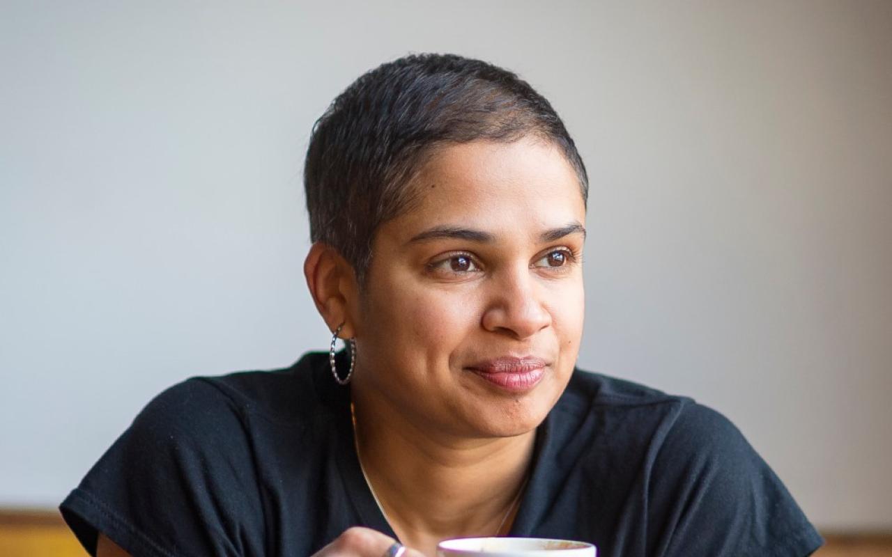 Photo of program faculty, Tanya Boteju, relaxed and smiling, leaning forward with coffee mug held in both hands