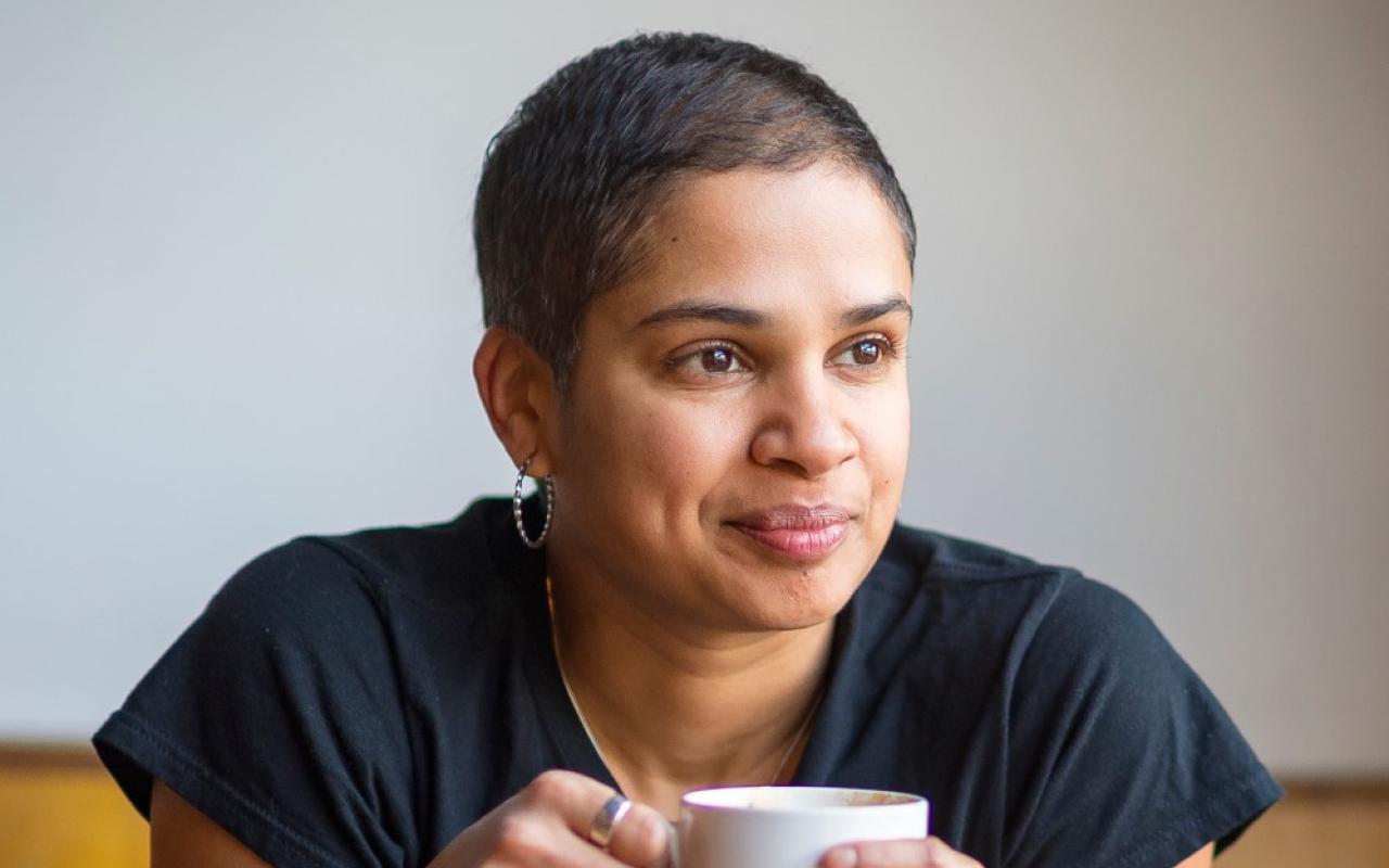 Photo of program faculty, Tanya Boteju, relaxed and smiling, leaning forward with coffee mug held in both hands