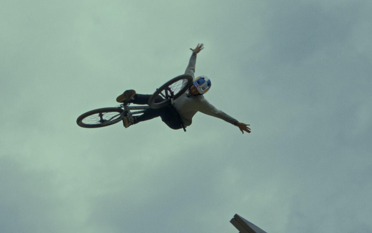 A fearless mann wearing a helmet taking a jump on his bike, spreading his arms like wings