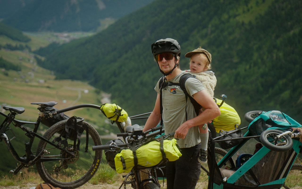 Man bikepacking in the mountains with a toddler on his back 