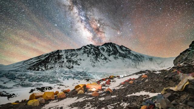Tents scattered across a snowy mountain peak with a star filled sky. 