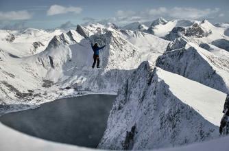 An athlete is walking on a slackline amongst snowcapped mountain peaks.