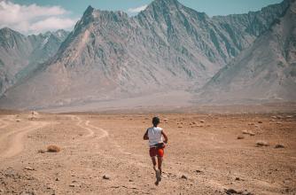 Athlete runs across sand and dirt in a dry mountain range. 