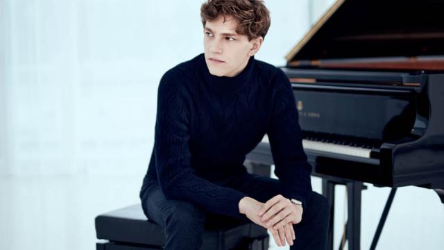 A man dressed in black is seated at a grand piano