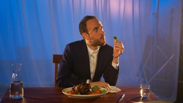 Michael Portnoy sits at a staged table comically holding broccoli.