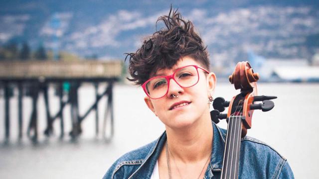 Cris Derksen on a beach seated in front of the pier with her Cello, to perform at Banff Centre 2018.