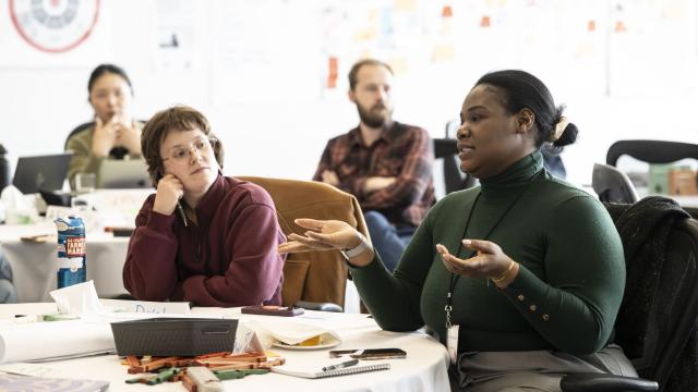 A group of people are listening to a woman speaking in a classroom