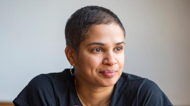 Photo of program faculty, Tanya Boteju, relaxed and smiling, leaning forward with coffee mug held in both hands