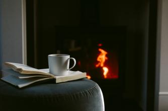 Cup of coffee on an open book in front of a fireplace.
