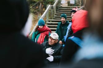 Elder Sykes speaks to a group on an outdoor staircase. Photo credit: Chris Amat