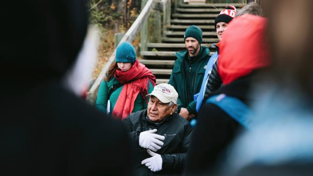 Elder Sykes speaks to a group on an outdoor staircase. Photo credit: Chris Amat