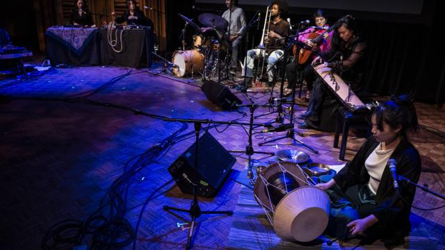 A group of musicians are performing on a darkened stage