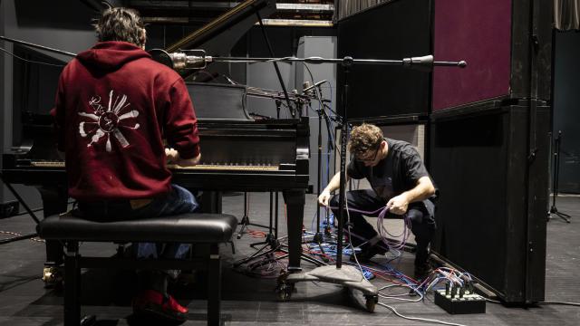An audio engineer participant adjusts some cables while another is seated at a piano