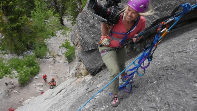 Filmmaker rock climbing with filming equipment