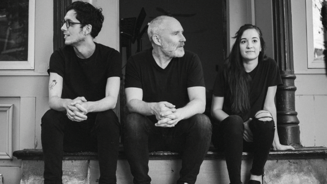 black and white picture of 3 persons seating on stairs wearing simple clothes