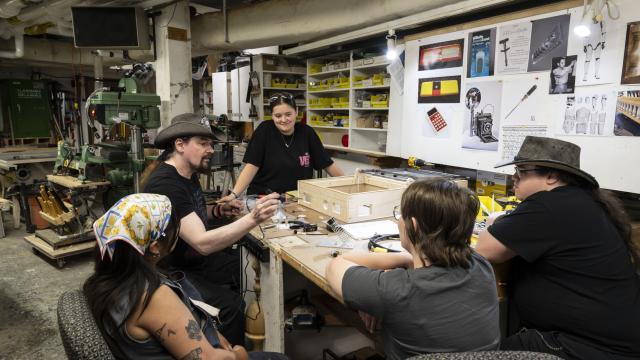 An instructor demonstrates a soldering tool to participants around a workbench in a props workshop.