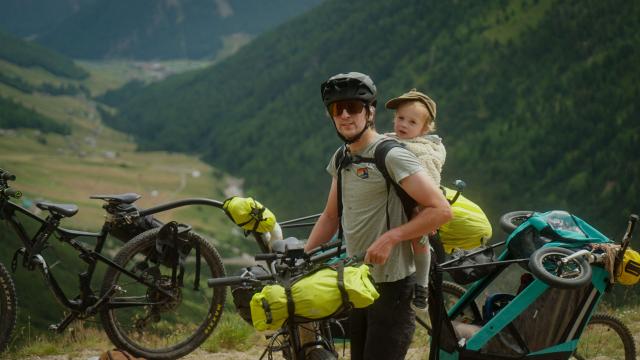 Man bikepacking in the mountains with a toddler on his back 