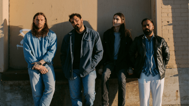 Four young men standing with a relax posture in front of a brick wall waring denim and 