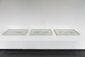 Three white frames sit on a shelf on the wall. Inside each frame is a different wire pattern with a rock or two.