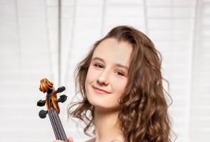 Anna Stube is holding a violin and looking towards the camera smiling