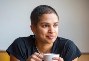 Photo of program faculty, Tanya Boteju, relaxed and smiling, leaning forward with coffee mug held in both hands