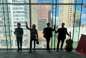 Members of Napoletano Quartet backlit in front of a large window showing a city scape behind them