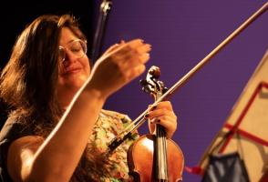 Alejandra pictured here with a purple background holding a violin. 