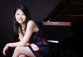Pei-Chen sits at the piano smiling at the camera. She has her hair down. 