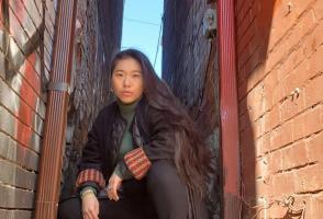 Rinchen Dolma is crouching down on a narrow sidewalk between two red brick walls marked with graffiti