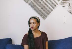 Photo of program faculty, Stephanie Comilang, sitting cross-legged on couch looking to her right