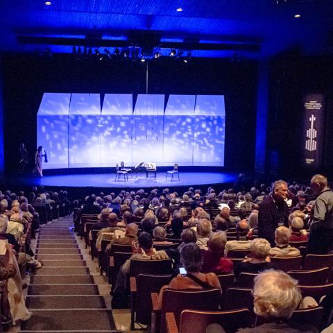 A picture of a theatre audience before a string quartet performance. 