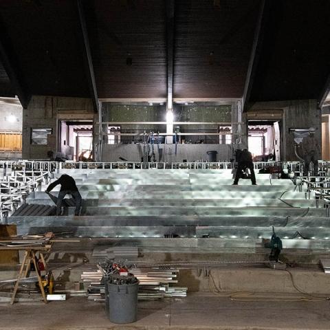 Construction crews work on the seating in a stripped down theatre. 