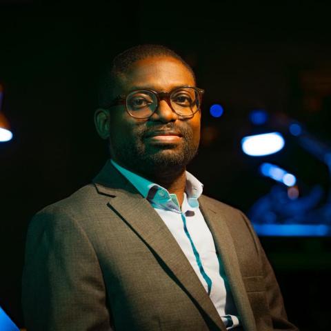 Dr Taiwo Afolabi, wearing a suit jacket and glasses, gazes directly into the camera