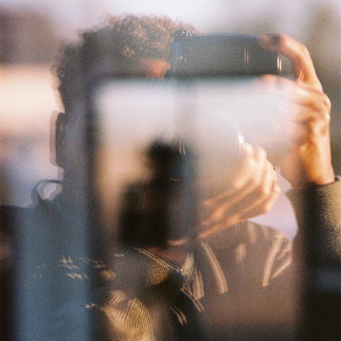 Men with camera shooting and being in the reflection of glass