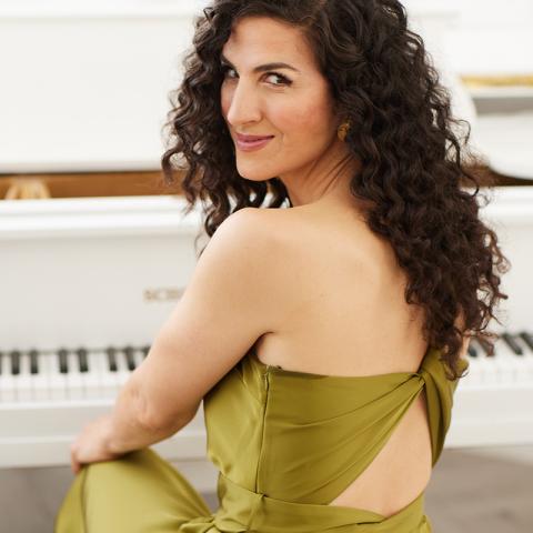 smiling woman seating facing back with long dark hair wearing green dress 