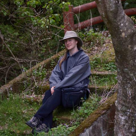 Cole Dorchester sitting outside on stairs overgrown with grass in a forest