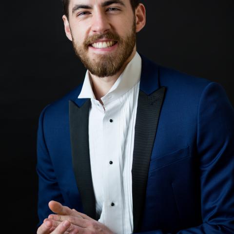 Man smiling directly at the camera in a blue dress jacket and tuxedo shirt