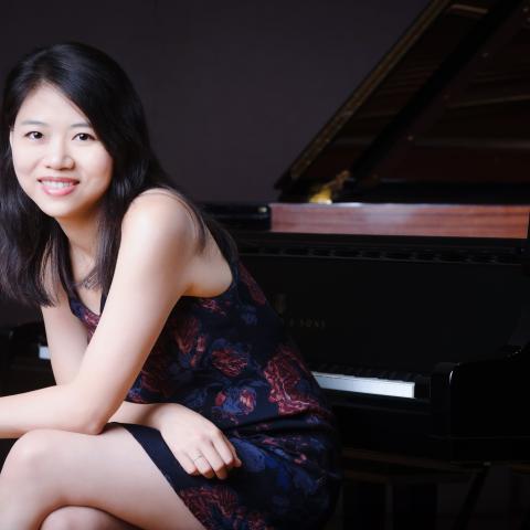 Pei-Chen sits at the piano smiling at the camera. She has her hair down.