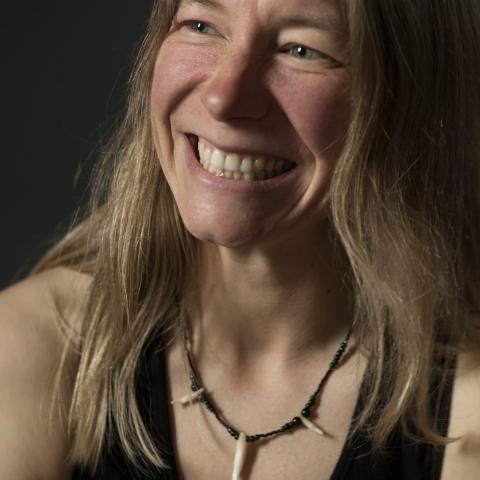 A close up photo of Kate in front of a black background. She is smiling.