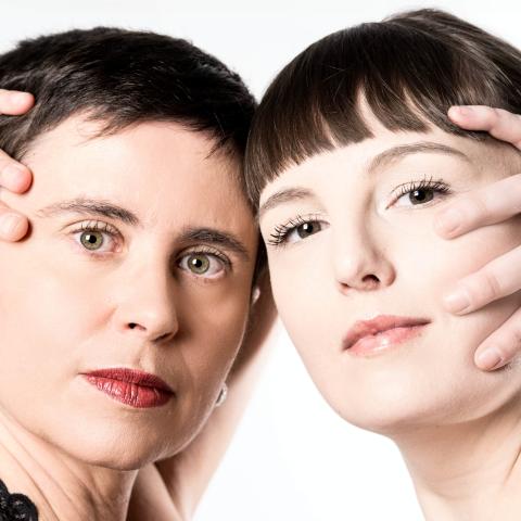 A headshot of Luciane and Katelyn with their hands on the face looking at us.