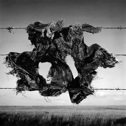 black and white image of a wire fence with tattered tarp tangled in the wires