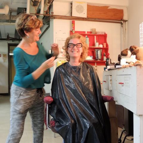 Blonde woman sits in hairdresser's chair looking very happy with her new hairdo.