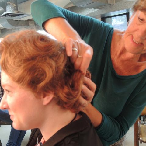 Carol Chambers pins up the back of a red wig on a woman