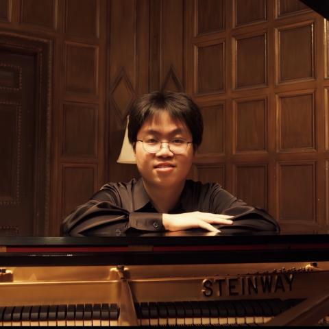 Man leaning over piano in black shirt looking at camera