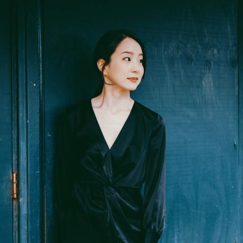 Woman in black dress standing in front of blue door looking towards the right of the camera