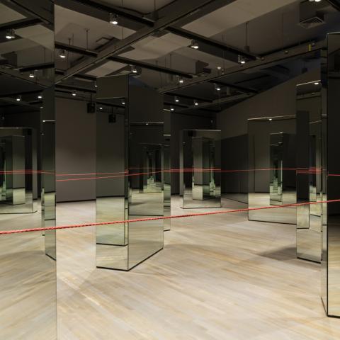 Multiple mirrors are standing in a room with a long red string connecting them all together.