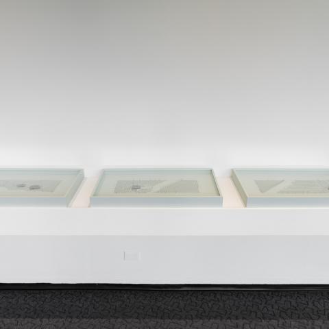 Three white frames sit on a shelf on the wall. Inside each frame is a different wire pattern with a rock or two.
