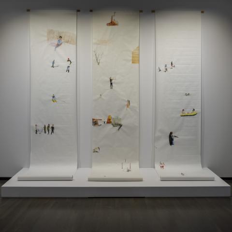 Three white paper scrolls hang from the wall. Each scroll has illustrations. 