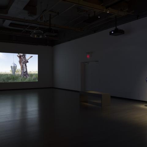 A video artwork is on the left hand side of the exhibition space and a mixed media sculpture hangs from the ceiling of the right side of the exhibition space.
